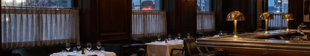 Upscale restaurant interior with dark wood paneling, chandeliers, and white tablecloths